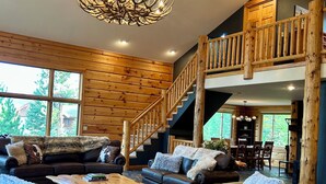 A spacious living area with a high ceiling, a chandelier, a wooden staircase, and a view of the outdoors. - Luxury Mountain Cabin: Hot Tub, Mtn Views, Game Room - Sleeps 10 - Winter Park (Fraser)