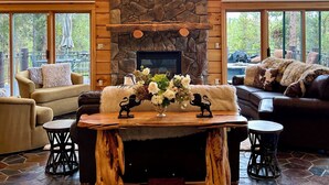 A spacious living room with a stone fireplace, large windows, and a chandelier. - Luxury Mountain Cabin: Hot Tub, Mtn Views, Game Room - Sleeps 10 - Winter Park (Fraser)