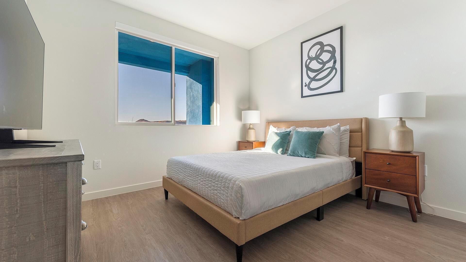 Una camera da letto con un letto, comodini, una lampada, una TV e una finestra con vista.