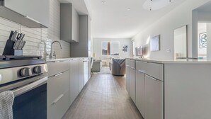 A modern kitchen with stainless steel appliances, a central island, and a view into the living area. - Landing | Incredible 1BD, Gym, Pool (Spring Valley)