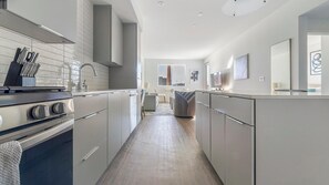A modern kitchen with stainless steel appliances, a central island, and a view into the living area. - Landing | Incredible 1BD, Gym, Pool (Spring Valley)