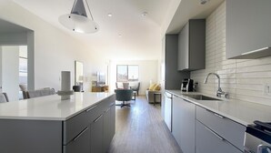 A modern kitchen with grey cabinetry, a central island, and a large window providing natural light. - Landing | Chic 2BD, Pool, Gym (Spring Valley)