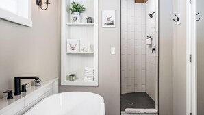 Une salle de bain moderne avec une baignoire blanche, une douche avec un mur recouvert de carreaux blancs, et une étagère avec des serviettes et des objets décoratifs.