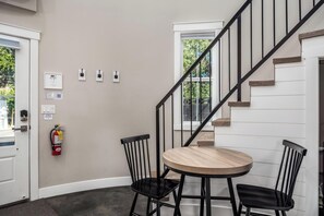 Ein Zimmer mit einem runden Holztisch, zwei schwarzen Stühlen, einem Feuerlöscher und einer Treppe mit schwarzer Geländer.