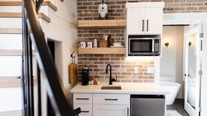 Une cuisine avec un mur en briques, des meubles blancs, un four à micro-ondes, une machine à café et un évier.