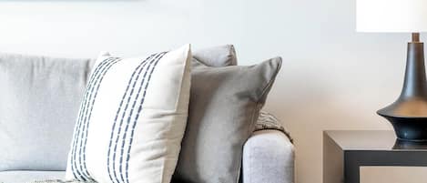 En moderne stue med en grå sofa, et mønstret plaide og et sort sofabord med en lampe.