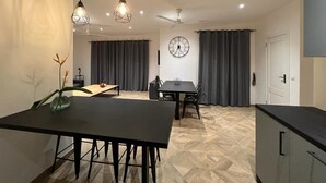 Eine moderne Küche mit schwarzem Arbeitsplatz, ein Essbereich mit Tisch und Stühlen, einer Wanduhr und einem Deckenventilator.