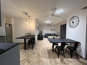 Una cocina moderna con refrigerador integrado, un comedor con mesa y sillas negras, y una sala de estar con sofá y un reloj decorativo en la pared.
