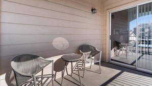 Un balcon avec des murs en bois de couleur claire, une porte vitrée, deux fauteuils en osier et une petite table.