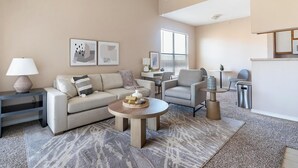 A modern living room with a sofa, armchair, coffee table, and a small side table. There is a window with blinds, a lamp, and a picture frame on the wall. - Landing | Beautiful 1BD, Pool, Gym (Fort Worth)