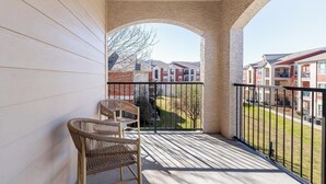 A balcony with wicker chairs, a view of a residential area, and a stone archway. - Landing | Beautiful 1BD, Pool, Gym (Fort Worth)