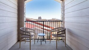 Un balcon avec deux fauteuils en osier et une petite table, une arche en pierre, et une vue sur les bâtiments en arrière-plan.