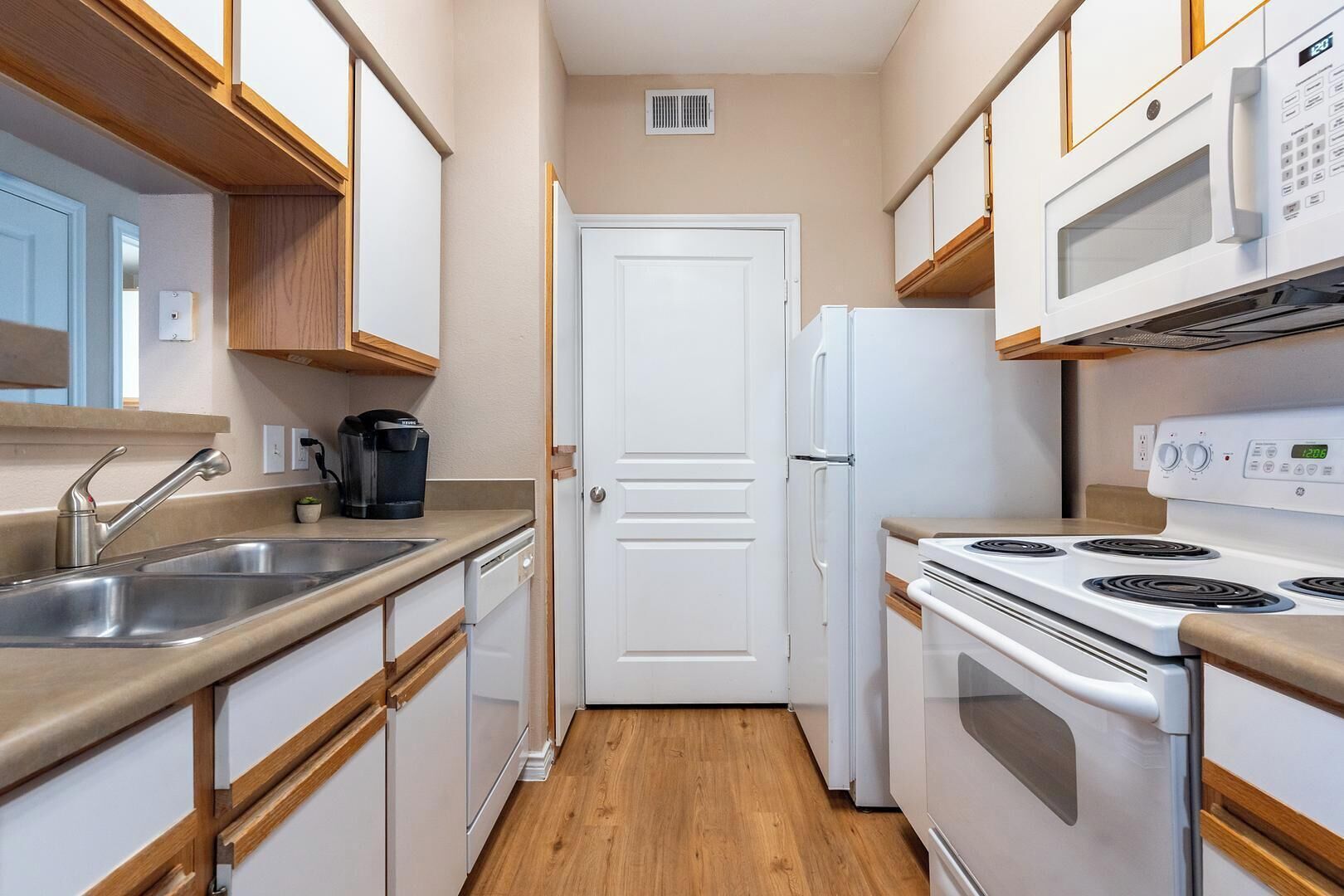 A compact kitchen with white cabinets, a stainless steel sink, a coffee maker, a white refrigerator, and a white stove.