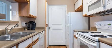 A compact kitchen with white cabinets, a stainless steel sink, a coffee maker, a white refrigerator, and a white stove.