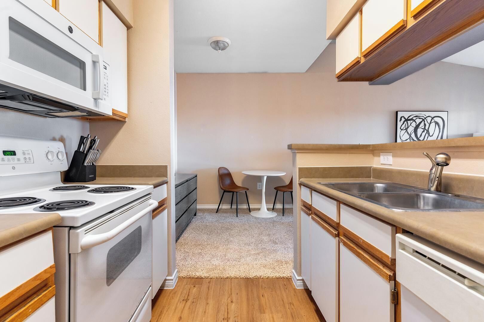 Cozinha compacta com fogão, micro-ondas, pia e um pequeno espaço de refeições com cadeiras.