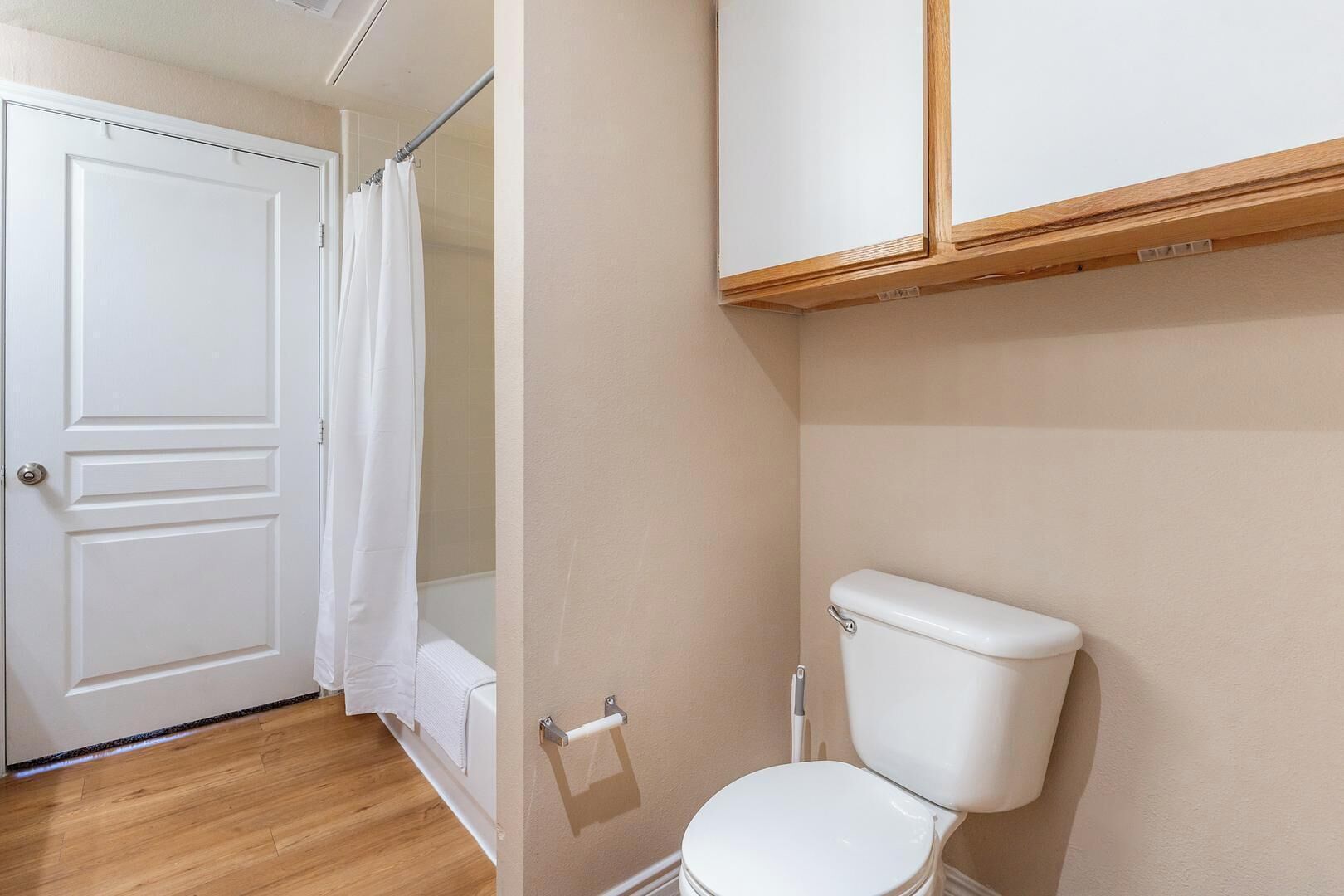 A bathroom with a white toilet, a shower curtain, and a door.