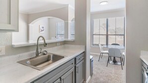 A modern kitchen with a stainless steel sink, a built-in oven, and a dining area with a table and chairs. - Landing | Beautiful 1BD, Gym, Pool (Houston)