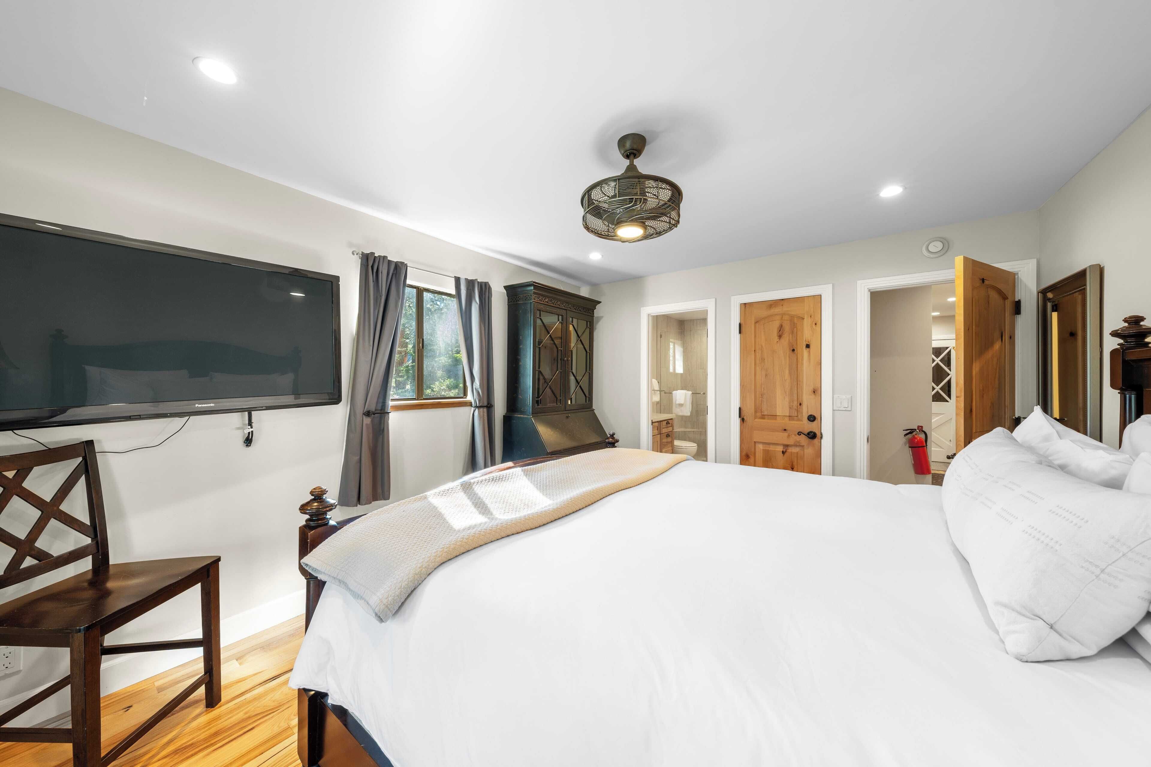 Un dormitorio con cama, televisor, armario y puerta que da a otra habitación.