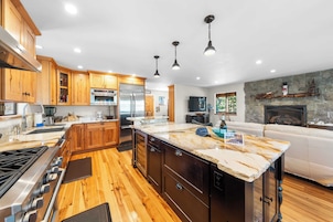 Una cocina moderna con armarios de madera, una isla grande, electrodomésticos de acero inoxidable y una chimenea de piedra.