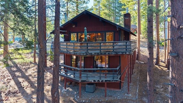 Eine zweistöckige Holzhütte mit Balkon, umgeben von Bäumen.