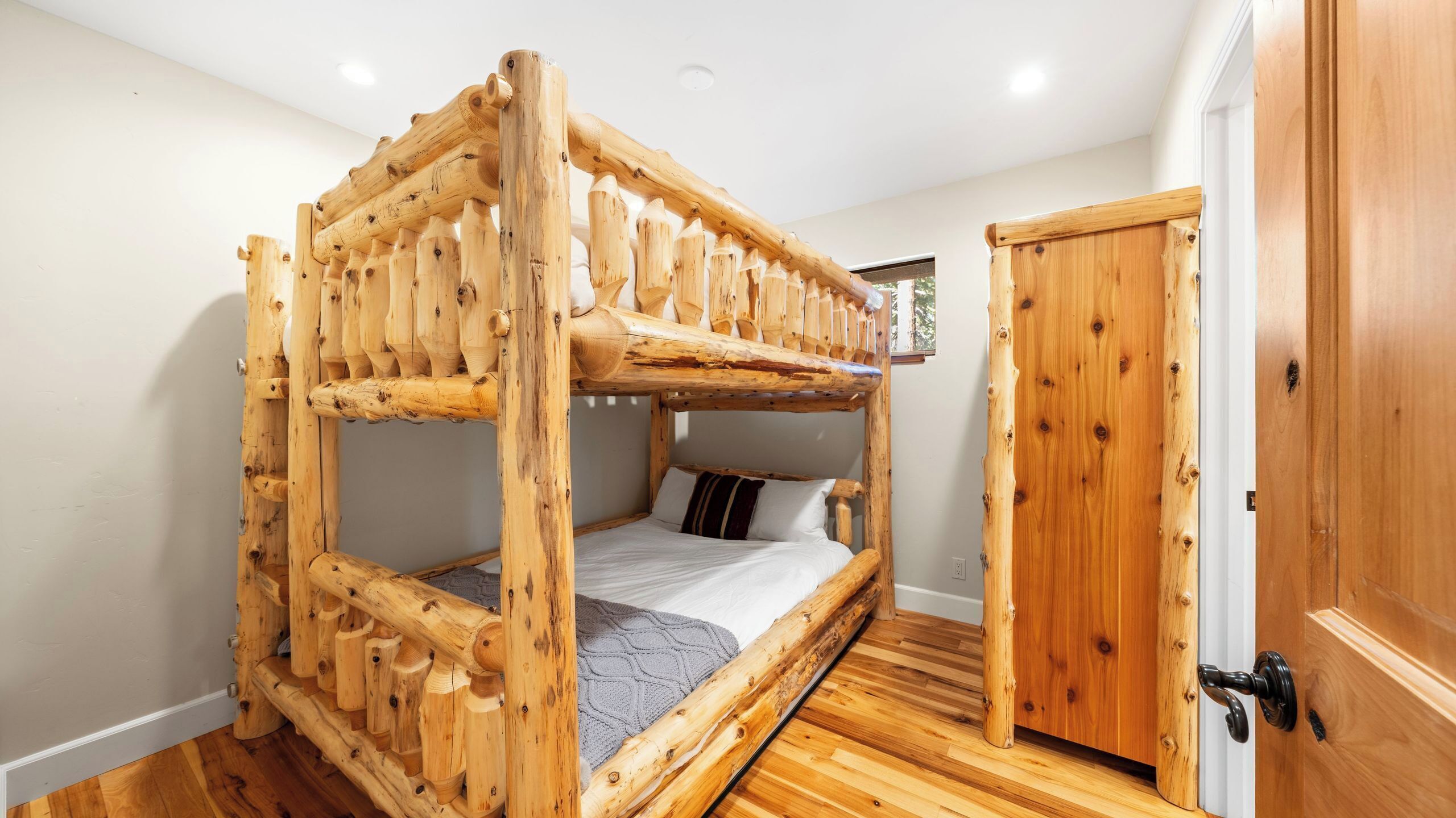 Ein Stockbett mit Holzrahmen, einer grauen Decke und einem Kopfkissen.