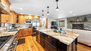 A modern kitchen with wooden cabinets, stainless steel appliances, a large island, and a stone fireplace.