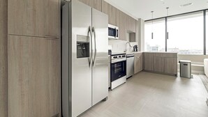 A modern kitchen with stainless steel appliances, wooden cabinets, and a large window offering a city view. - Landing | Stylish 1BD in Fountain Heights (Birmingham)