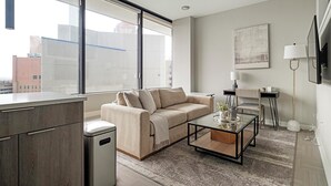 A modern living room with a sofa, coffee table, and a view of the city through large windows. - Landing | Stylish 1BD in Fountain Heights (Birmingham)