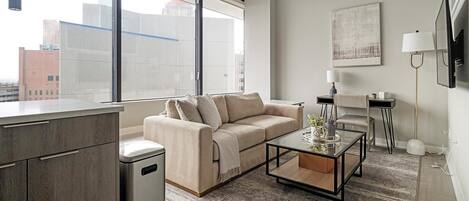 A modern living room with a sofa, coffee table, and a view of the city through large windows.