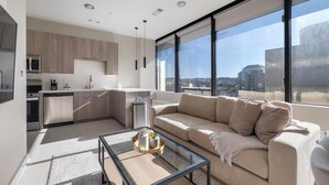 Een modern appartement met keuken, een zithoek met een bank en grote ramen met uitzicht op de stad.