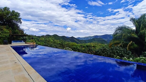 Uma piscina infinita azul límpida com vista para colinas verdejantes e um céu parcialmente nublado.