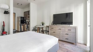 A bedroom with a large bed, a dresser with drawers, a television, and a small table with a plant.