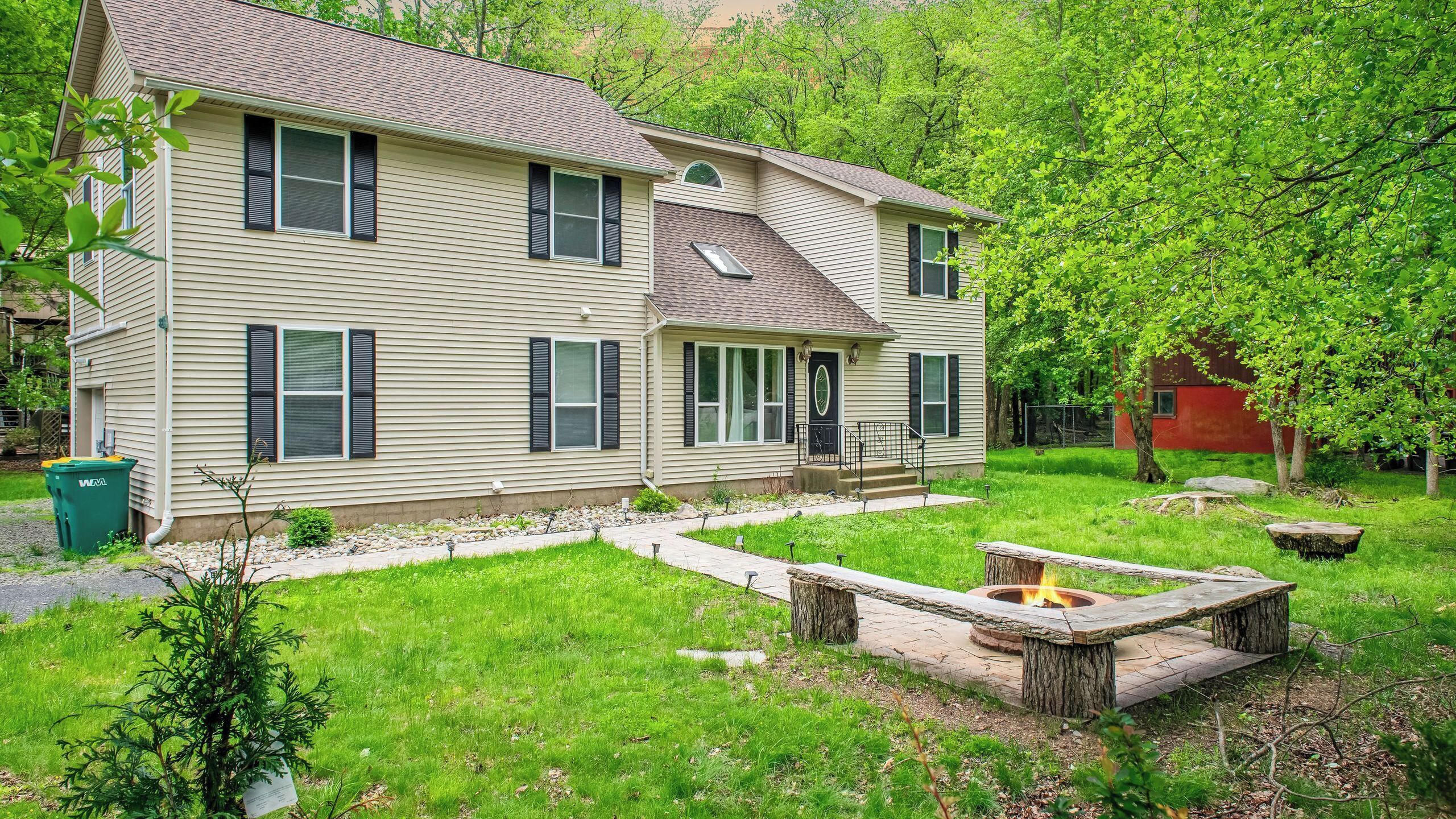 A two-story house with a front porch, a fire pit, and a well-maintained lawn.