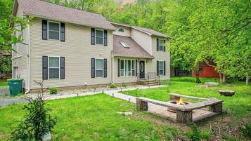 A two-story house with a front porch, a fire pit, and a well-maintained lawn.