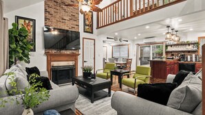Amplia sala de estar con chimenea, comedor y cocina con armarios de madera.
