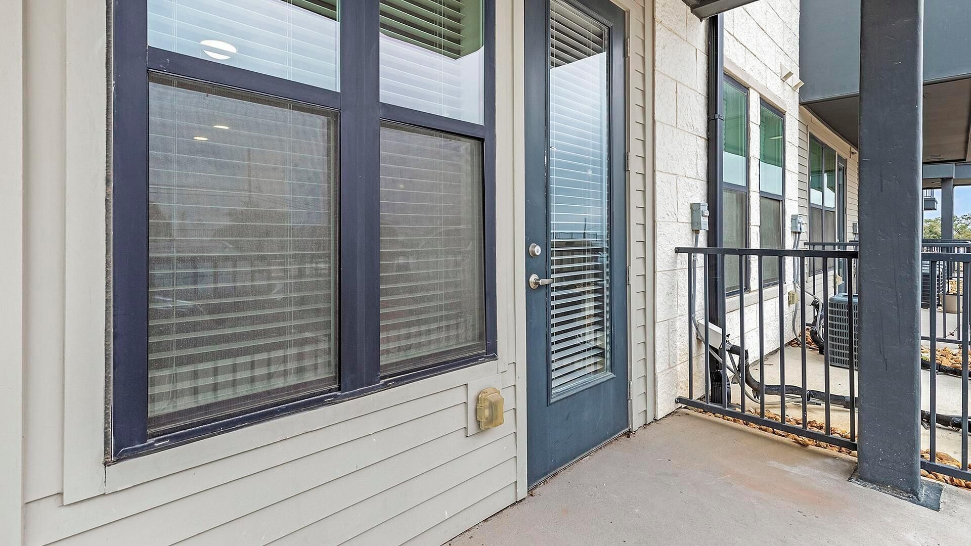 En bygning med store vinduer, en dør og en balkon med gelænder.