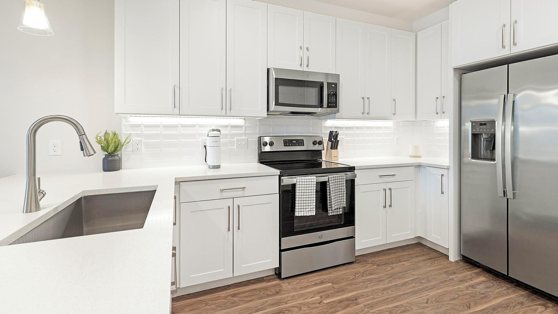 A modern kitchen with white cabinets, stainless steel appliances, and a wooden floor.