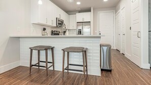 A modern kitchen with white cabinets, a stainless steel refrigerator, and two bar stools.
