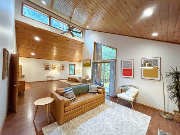 Un salon spacieux doté d’un plafond en bois, de grandes fenêtres, d’un canapé, d’un fauteuil et d’un lampadaire.