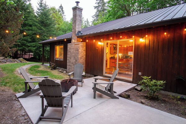 A wooden cabin with a stone chimney, outdoor seating, and a pathway leading to the entrance.