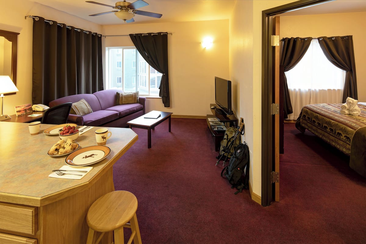 A hotel room with a dining area, a sofa, a TV, and a bed.