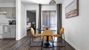 A modern kitchen with grey cabinets, a dining area with a round table and yellow chairs, and a large window with curtains. - Landing | Amazing 2BD, Gym, Pool (Austin)