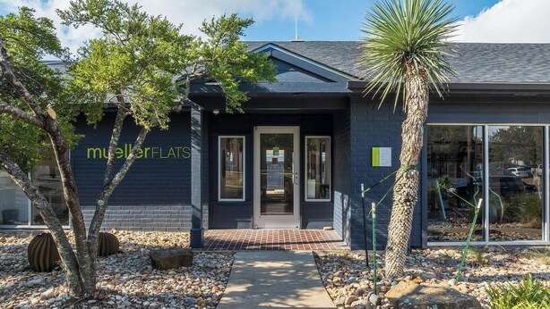 A modern building with a dark facade, a clear glass entrance, and a sign reading "mullerFLATS". - Landing | Amazing 2BD, Gym, Pool (Austin)
