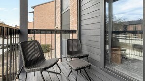 A balcony with two wicker chairs and a small table, overlooking a parking area and buildings. - Landing | Beautiful 1BD, Pool, Gym (Austin)
