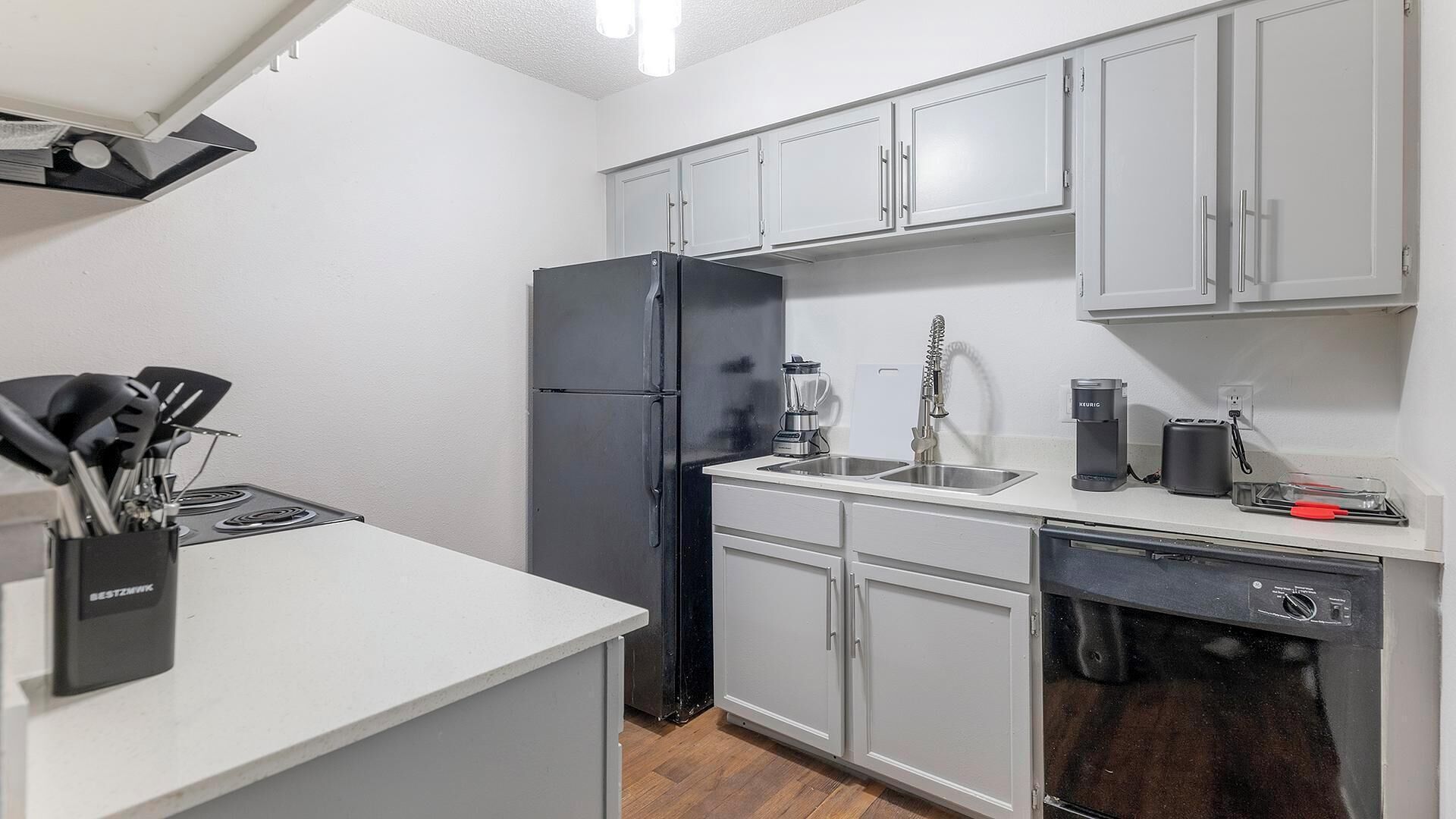 A compact kitchen with white cabinets, a black refrigerator, a sink, and a coffee maker.