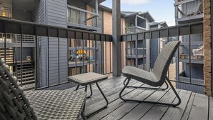 A balcony with wicker furniture, a view of neighboring buildings, and a metal railing.