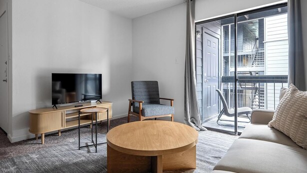 A modern living room with a flat-screen TV, a wooden coffee table, a blue armchair, and a sofa. - Landing | Chic 1BD, Gym, Pool (Austin)