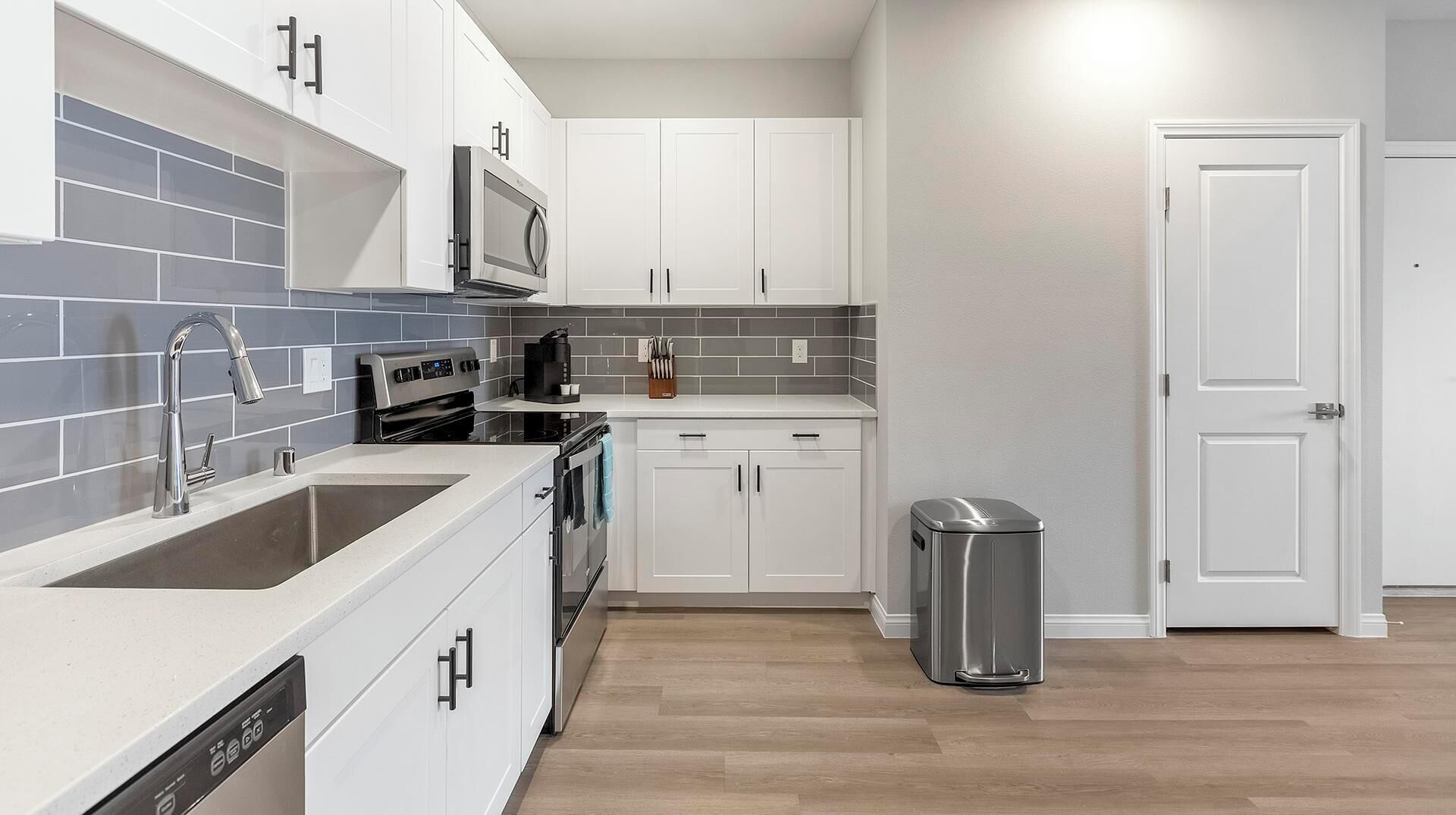A modern kitchen with white cabinets, a stainless steel sink, a microwave, and a dishwasher.