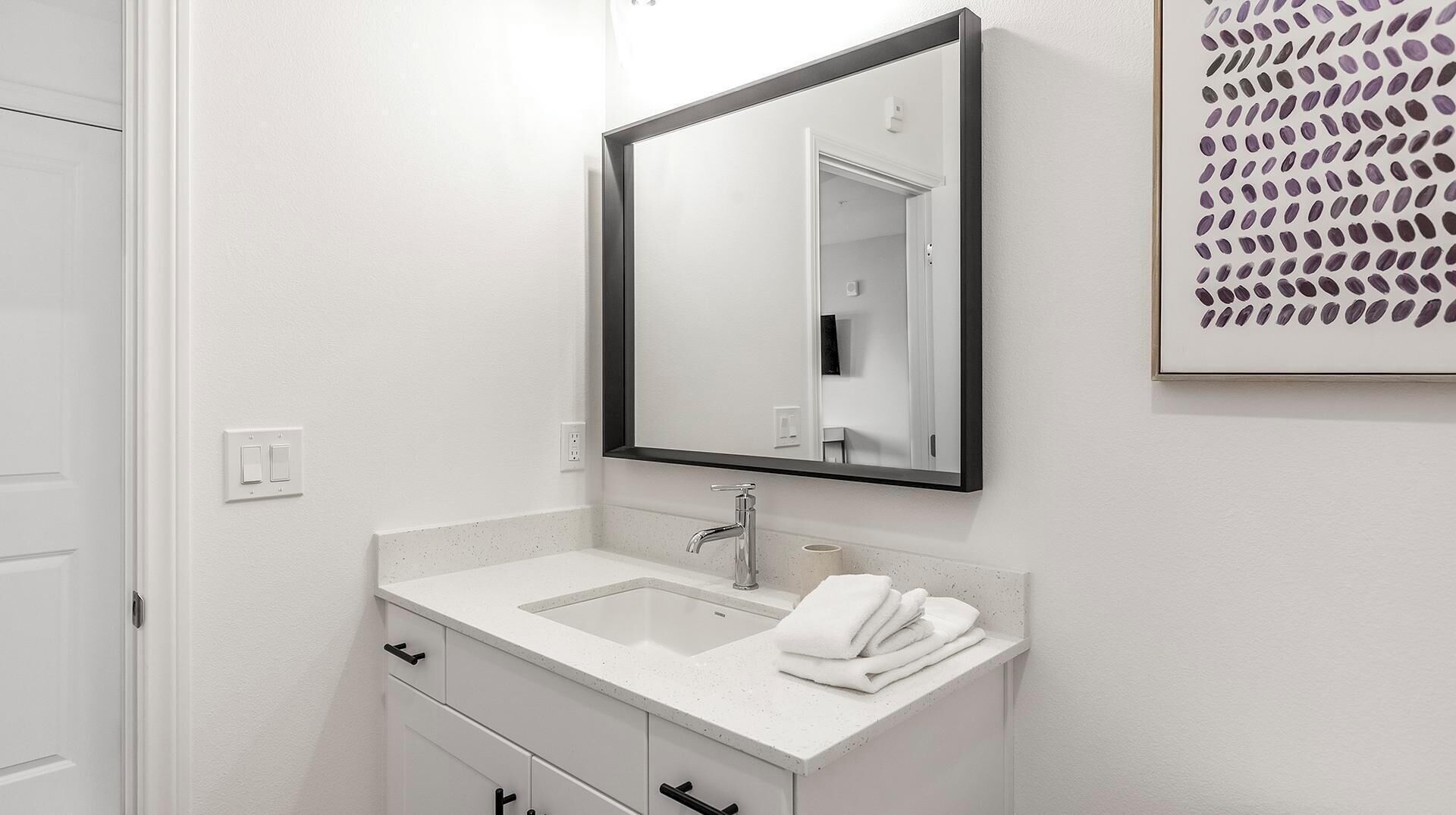 A bathroom with a white sink, a mirror, and a towel rack.