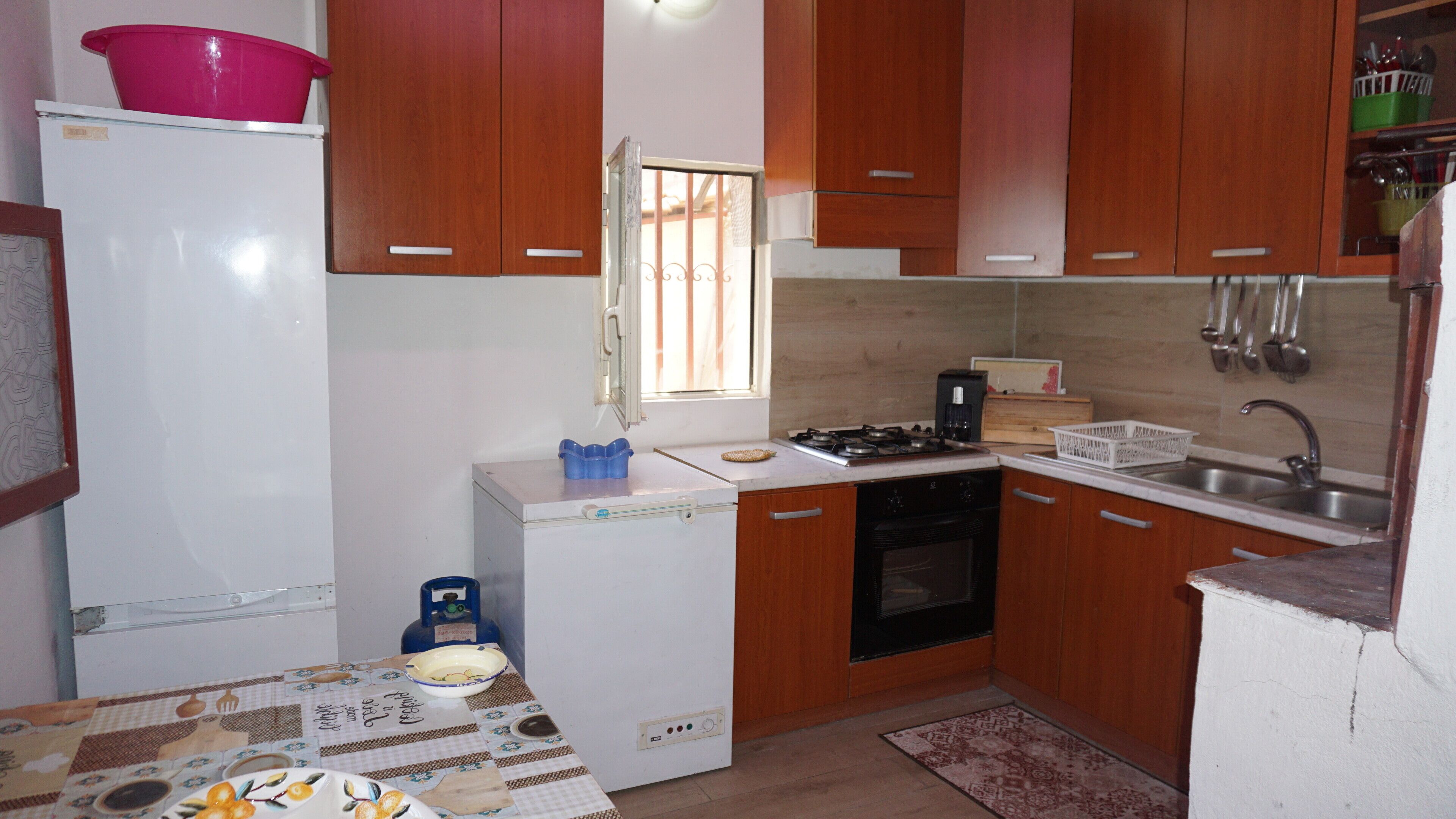 Une cuisine de taille réduite, avec des meubles en bois, un réfrigérateur blanc, une cuisinière à gaz et un évier.